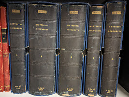 A photograph of the 5 volumes of transcripts that were smuggled to LSE Library. They have a black binding and are in blue coloured boxes. They read "Matteotti documents" along the spine. 