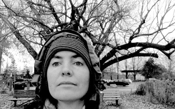 Black and white photo of me wearing a hooded coat in front of tree branches. The framing makes it look like the branches are growing from my head like a macabre crown.