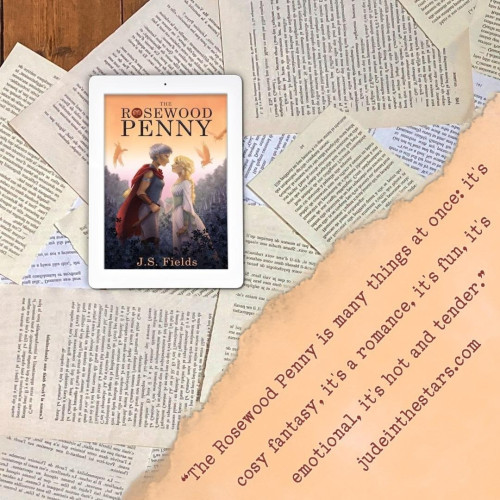 On a backdrop of book pages, an iPad with the cover of The Rosewood Penny by J.S. Fields. In the bottom right corner of the image, a strip of torn paper with a quote: "The Rosewood Penny is many things at once: it's cosy fantasy, it's a romance, it's fun, it's emotional, it's hot and tender." and a URL: judeinthestars.com.