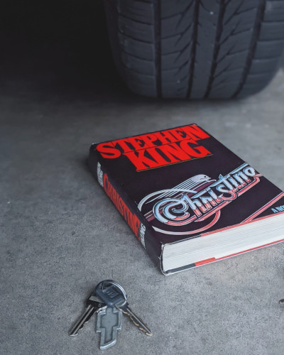 A view from behind a tire, the book, Christine by Stephen King, and a set of keys.