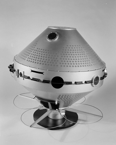 Silver and black satellite mockup with middle cylinder as largest diameter and cylindrical cones on to and bottom cut off for flat small circle top and bottom with black stand at bottom. Black and white image light background.