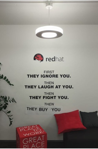 This picture is taken when IBM brought Red Hat. Someone at the Red Hat office updated their wall.

We see the Red hat shadow man logo.

The following text is printed on the wall:

First, they ignore you.
Then
They laugh at you.
Then
They FIGHT you.
Then
They buy you.