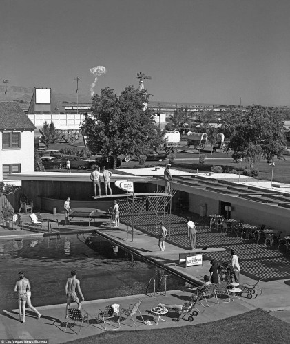 Photo of swimmers at a hotel swimming pool looking towards a mushroom cloud from a nuclear test in Las Vegas