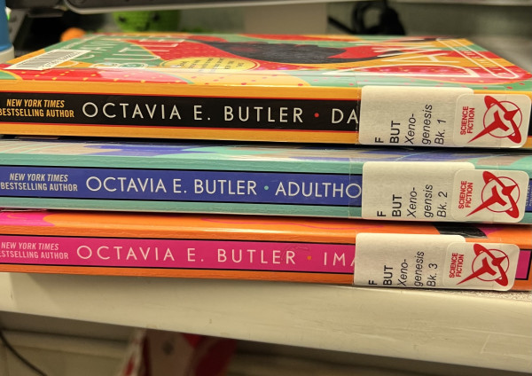 Stack of three library paperback books by Octavia E. Butler labeled Xenogenesis 1,2, and 3: Dawn, Adulthood, and Imago.