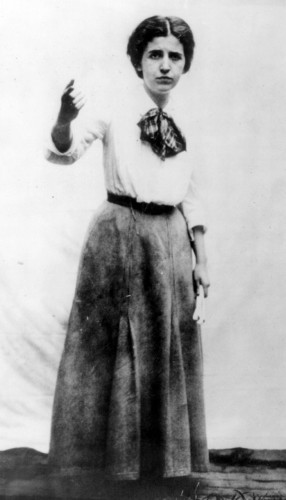 Black and white portrait of Elizabeth Gurley Flynn in a white blouse, scarf and dark skirt, pointing a finger emphatically in what looks like a pause during a speech. Public Domain, https://commons.wikimedia.org/w/index.php?curid=456361