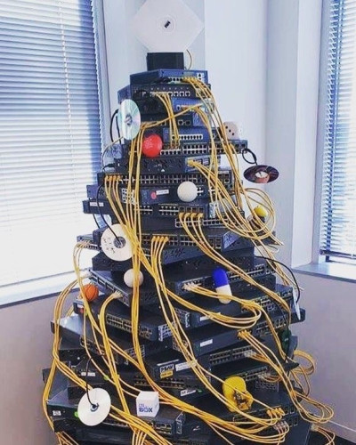 A stack of network switches arranged in the shape of a tree, with yellow cables instead of tinsel, and CDs instead of baubles.