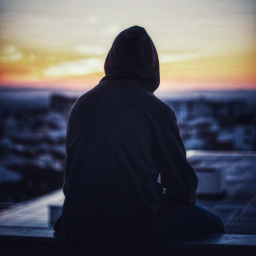 The silhouette of a hooded person, staring at sunset horizon 