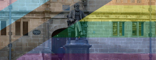 Photograph of the statue of Charles Darwin in Shrewsbury viewed through progress pride flag-coloured filter.