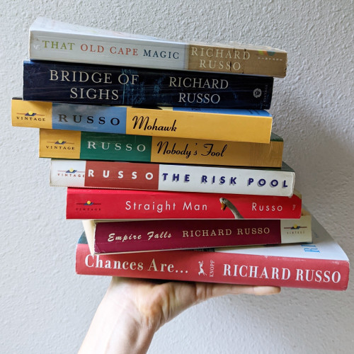 My hand, holding a stack of books by Richard Russo.