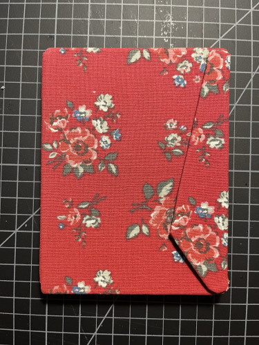 Red fabric ebook case with floral pattern on a grid surface.
