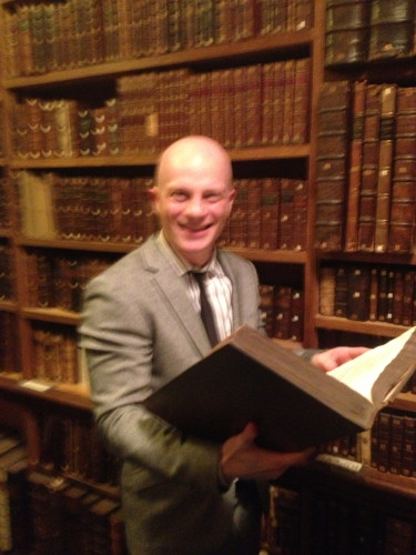 Me standing in Cambridge, 2013, in Pepys Library (Magdalene College) smiling while holding a big book.
