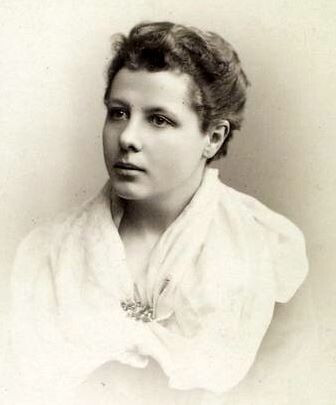 A black and white photographic portrait of Annie Besant. She is looking up and to the viewer's left, a wistfully neutral expression on her face. Her brown hair is pulled back away from her face and she wears a white shawl. 