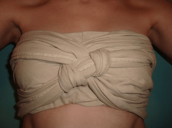 Photo of a woman replicating how to wear a Roman strophium. A white piece of fabric, probably linen, was folded and knotted in place in a criss-cross at the cleavage, a secure and elegant fashion.