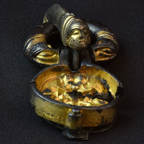Photo of silver gilded buckle with a human face over a cup. Source: Västergötlands Museum.